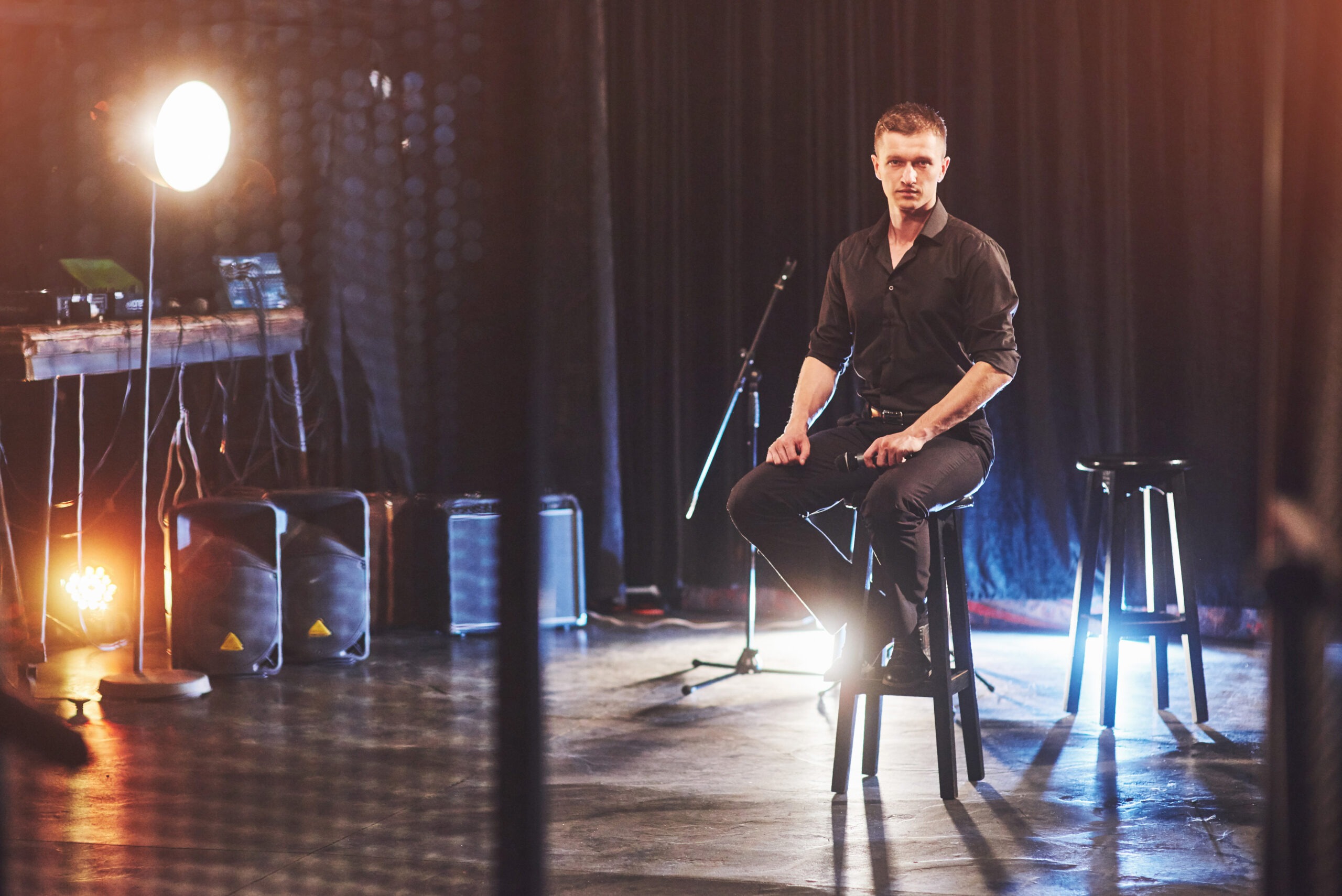 Male Musician Sitting on a Stool Performing on Stage with a Microphone