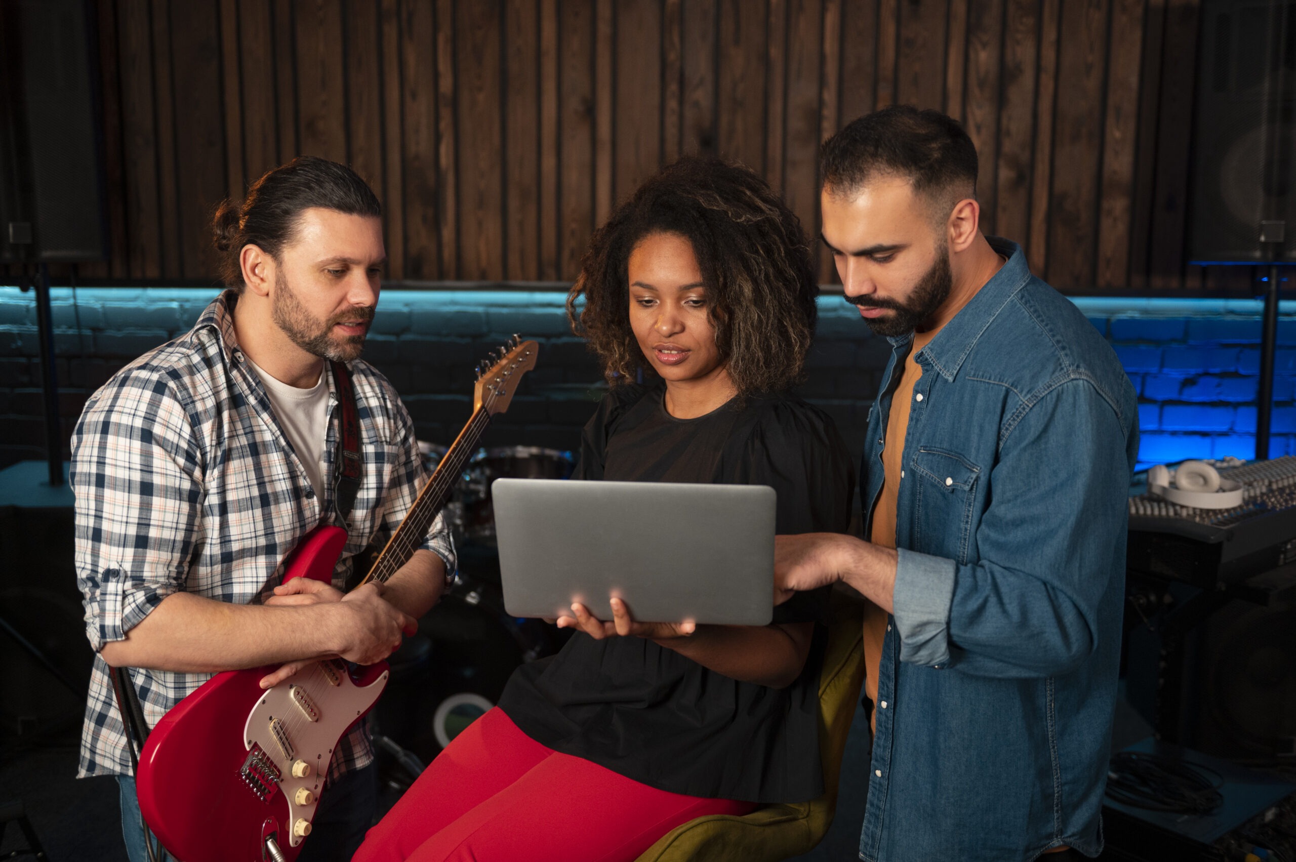 Three Musicians Reviewing Something on a Laptop Inside a Studio