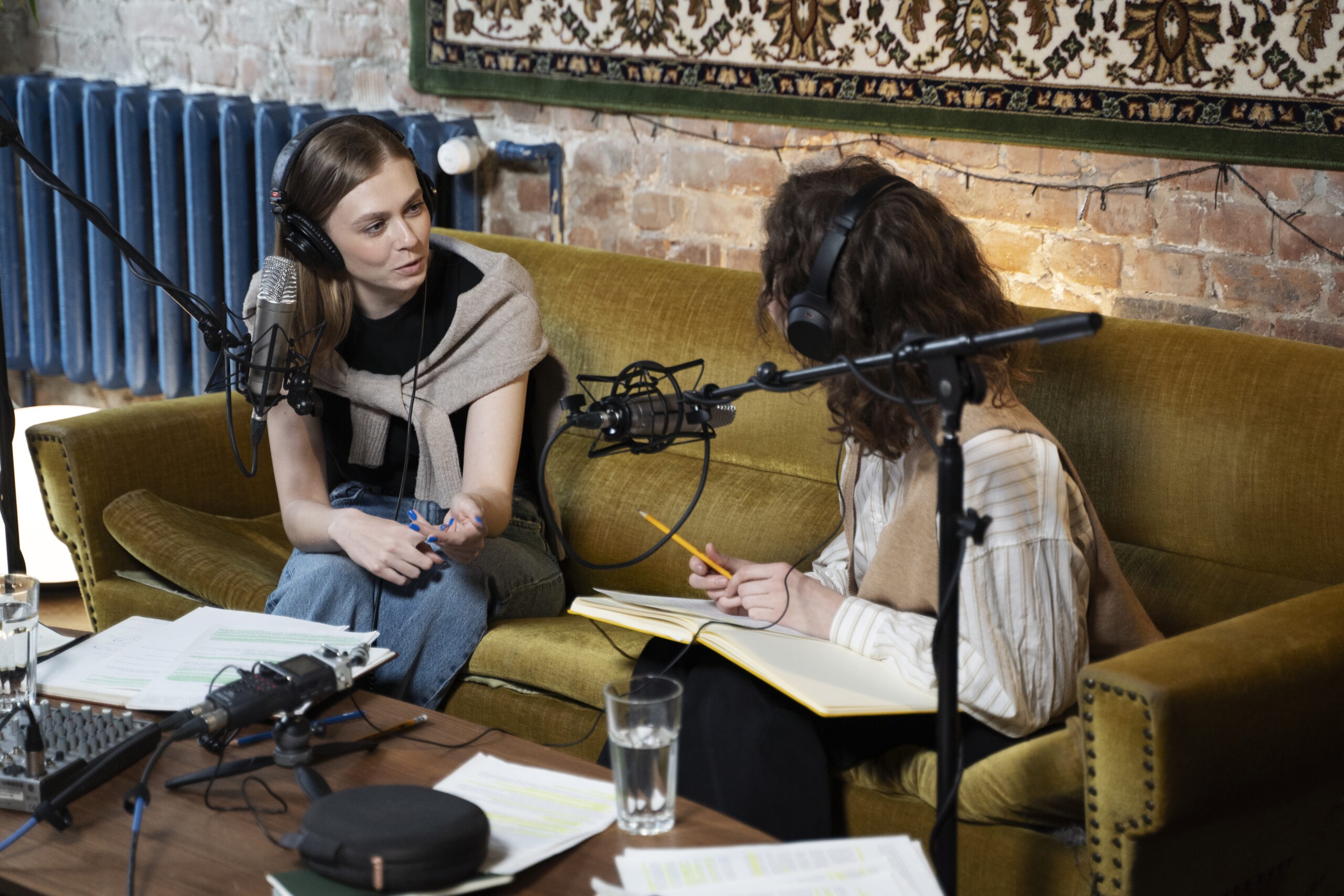 Two Women Sitting on a Sofa in a Cozy Studio Environment Discussing Notes and Planning Music-Related Work